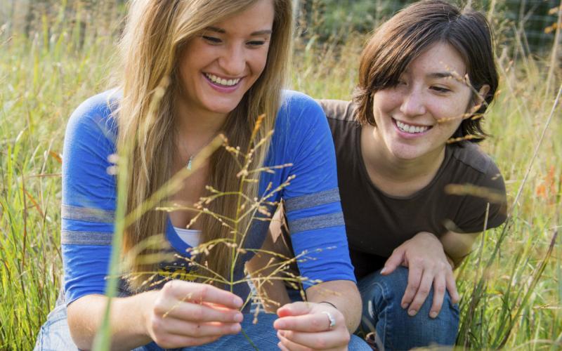 two female youth inspecting a plant in a pasture