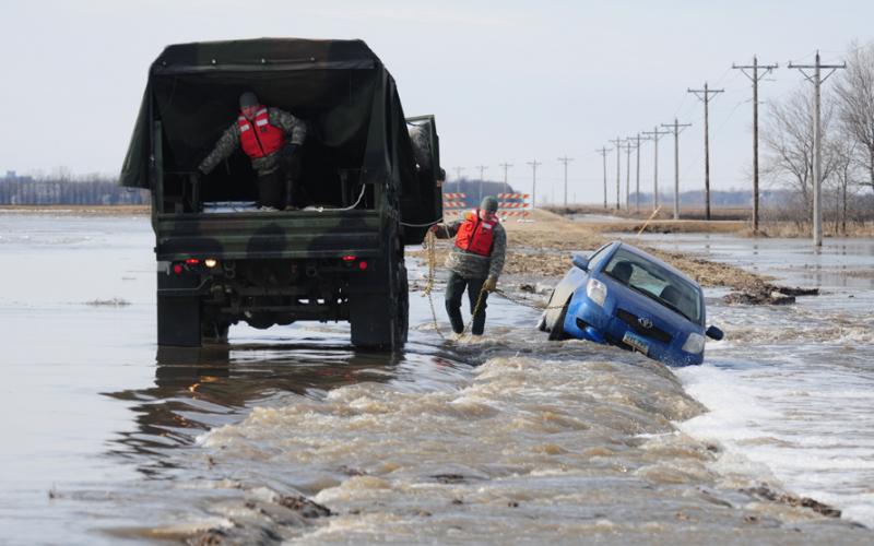 A car being towed a flooded, washed out gravel road by a national guard truck. Photo by Senior Master Sgt. David H. Lipp, U.S. Department of Defense