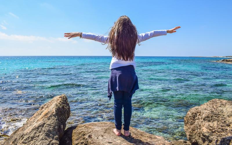 young woman standing by the oceanside with arms outstretched
