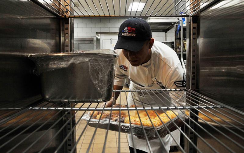 kitchen worker removing a tray of food for a large refrigerator