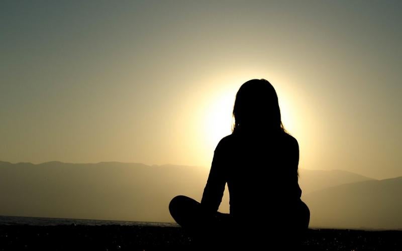 silhouette of a woman meditating. sunset in the background.
