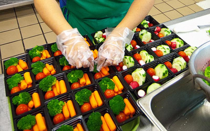 woman wearing gloves preparing servings of vegetables. USDA Photo Courtesy of Bob Nichols.