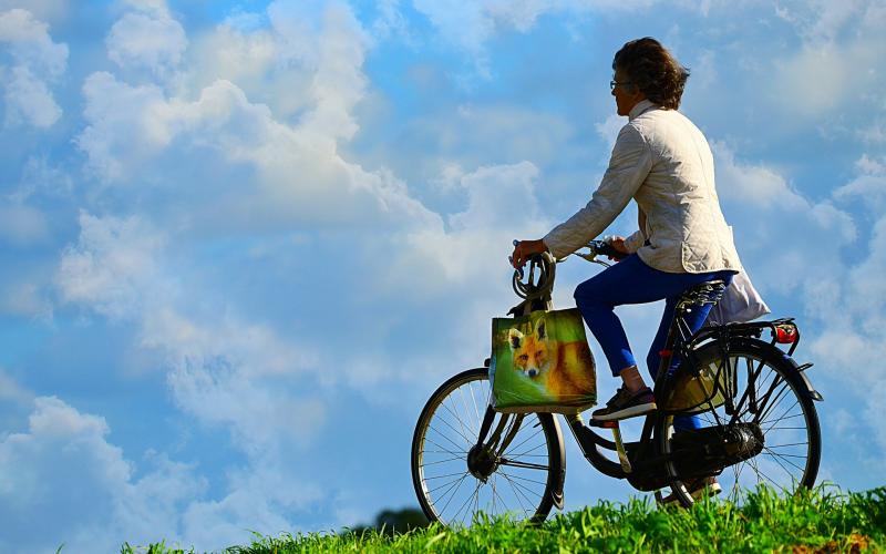 A woman riding a bike on a green hill. A bright blue sky with patchy white clouds is in the background.