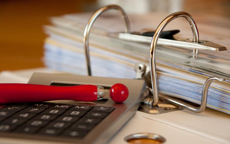 A pen and calculator sitting next to an accounting binder.