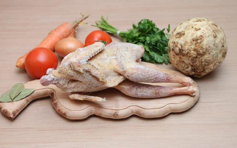 An uncooked, seasoned whole chicken on a cutting board with fresh vegetables.