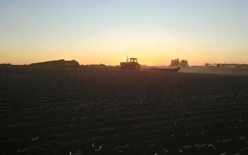 Tractor preparing a soybean field for planting at twilight.