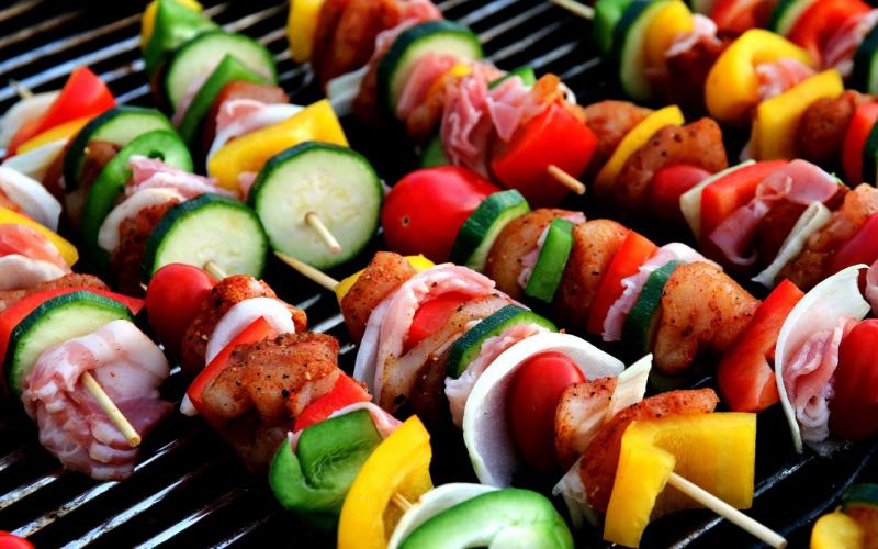 Several kabobs with pieces of fresh vegetables and lean meats cooking on a grill.