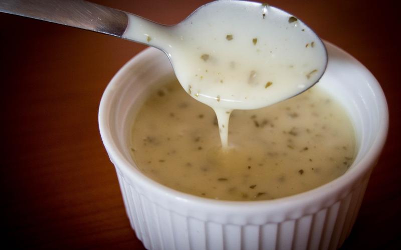 A spoon lifting creamy, white salad dressing from a whit ramekin.