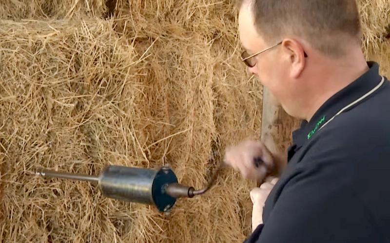 A man drilling a core sampler into the side of a hay bale.