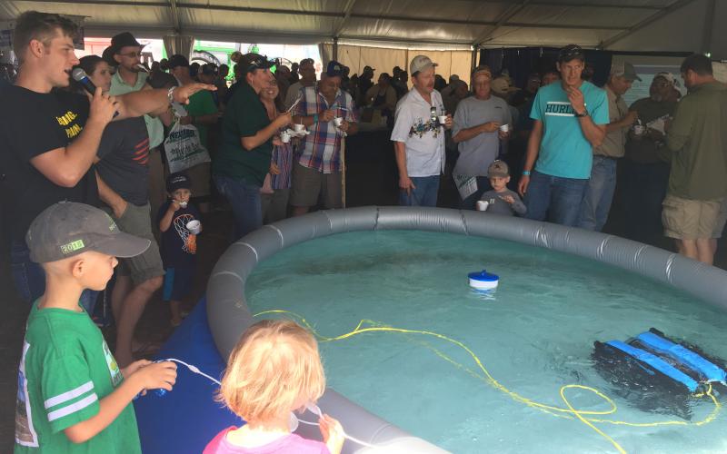 A young boy operating an underwater drone in large pool in front of a crowd of onlookers.