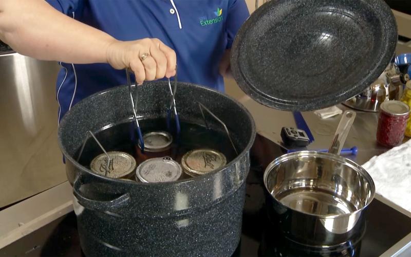 A woman safely placing a can of salsa into a water bath canner.