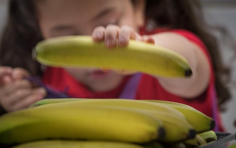 A young girl taking a banana from a tray of uneaten food.