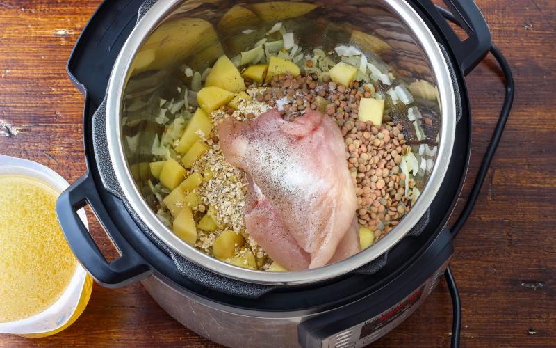An instant pot pressure cooker with chicken, butter, vegetables, and seasoning inside.