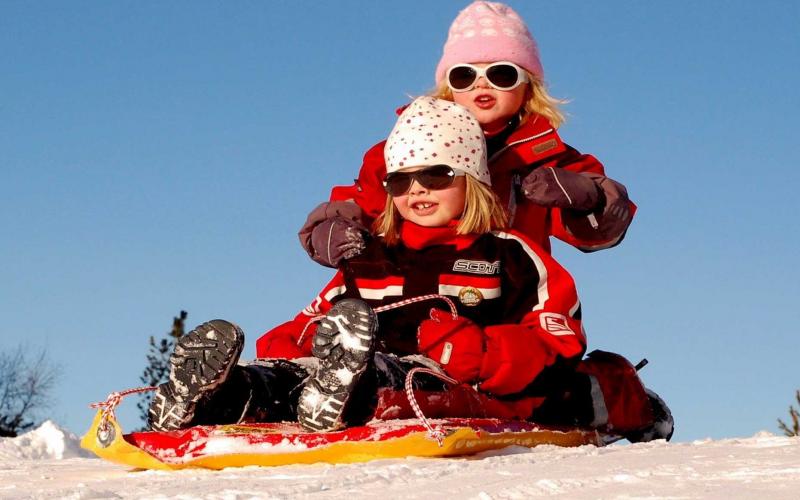 Two young girls in winter clothing riding on a sled.
