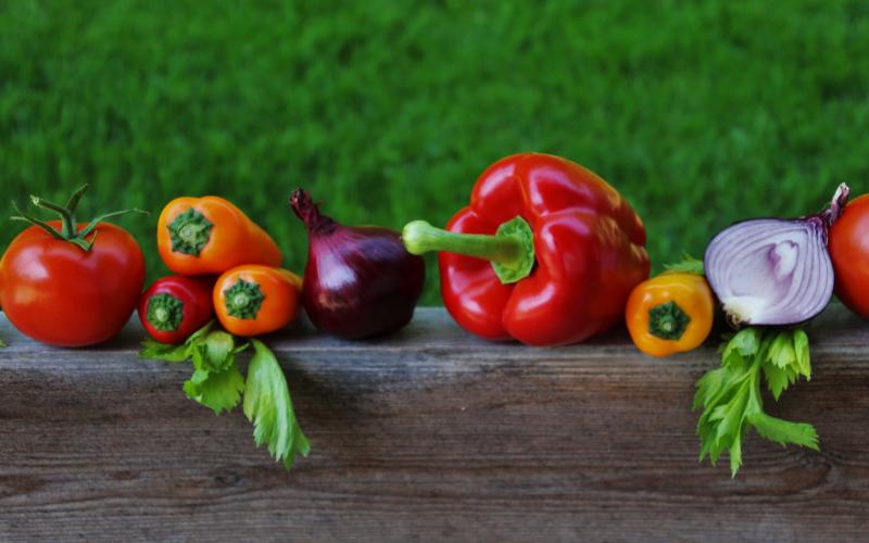 A variety of fresh, garden vegetables sitting on a wooden fence.
