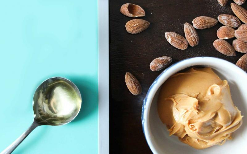 Almonds, a tablespoon of oil, and almond butter sitting on a countertop