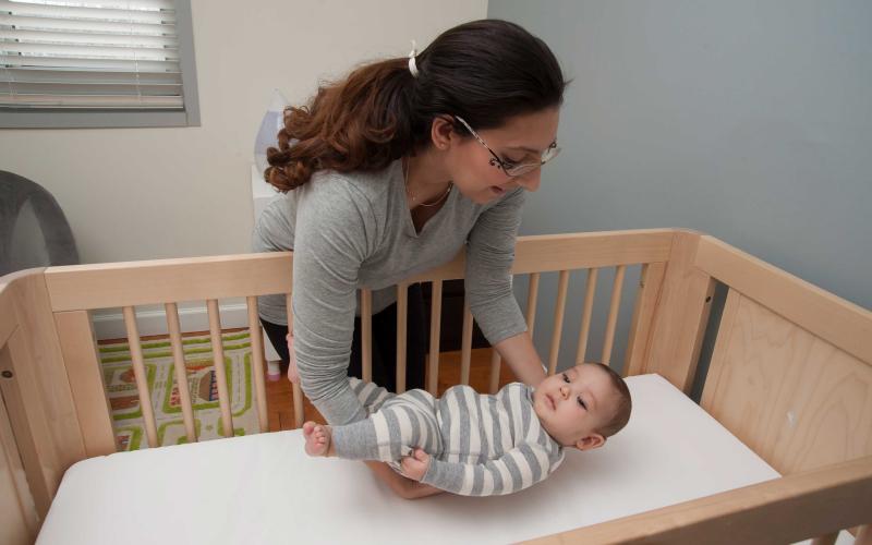 A young woman carefully placing her infant child in a crib on his back.