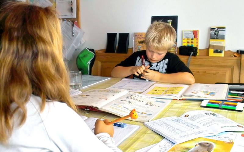 A young male student studying at the kitchen table with an older sister.