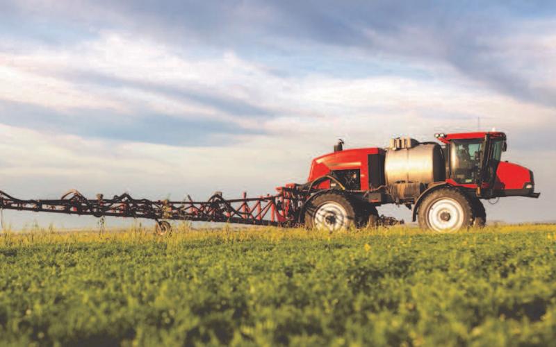 A red sprayer in a green field with a cloudy sky in the background.