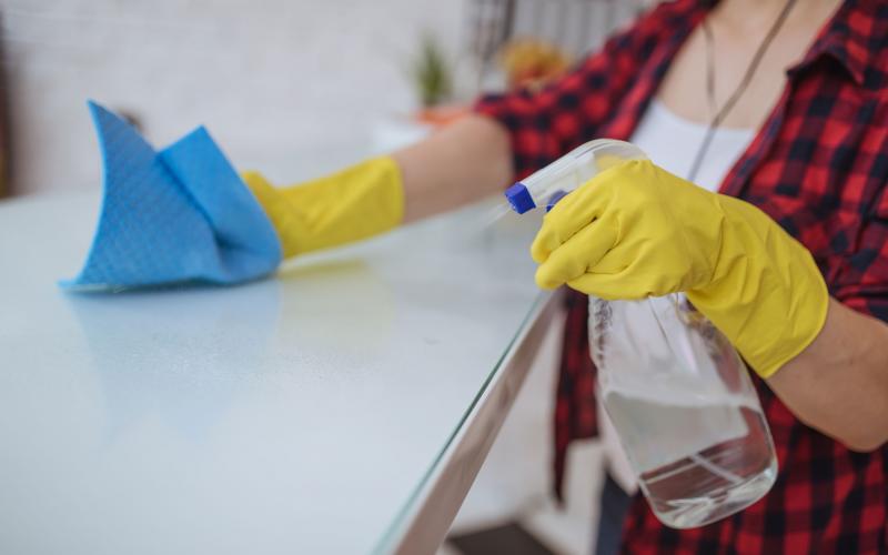 A woman wearing yellow, rubber gloves, spraying a homemade bleach solution on a kitchen counter.