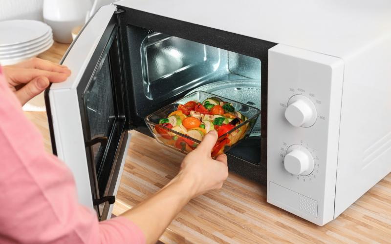 Woman putting bowl with vegetables in microwave oven.