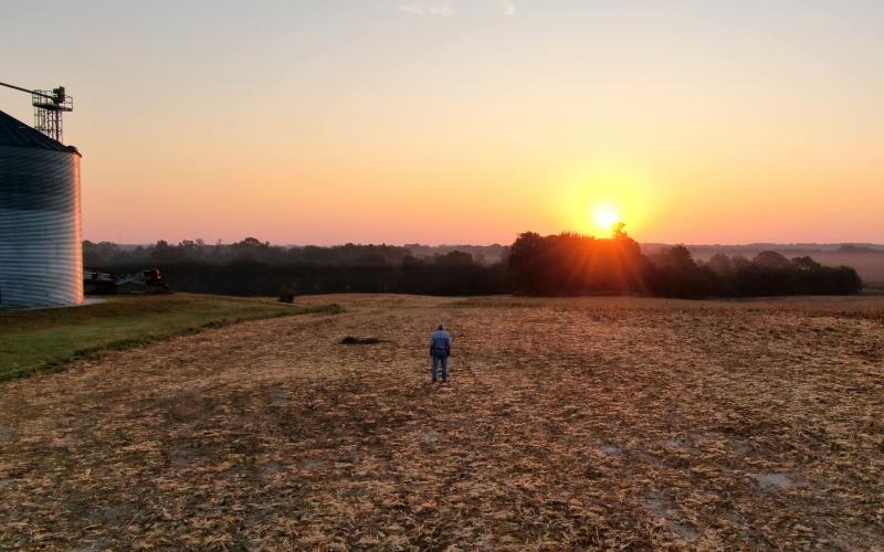 A farmer watching the sun rise in a bare, unplanted field.