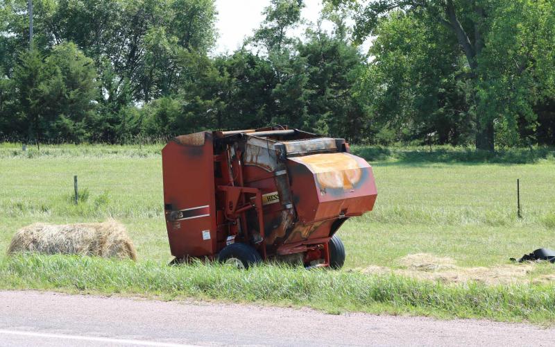A red, round hay baler that has been burned up from a fire.