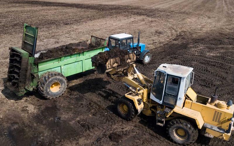 A loader depositing soil into a trailer being pulled behind a tractor.