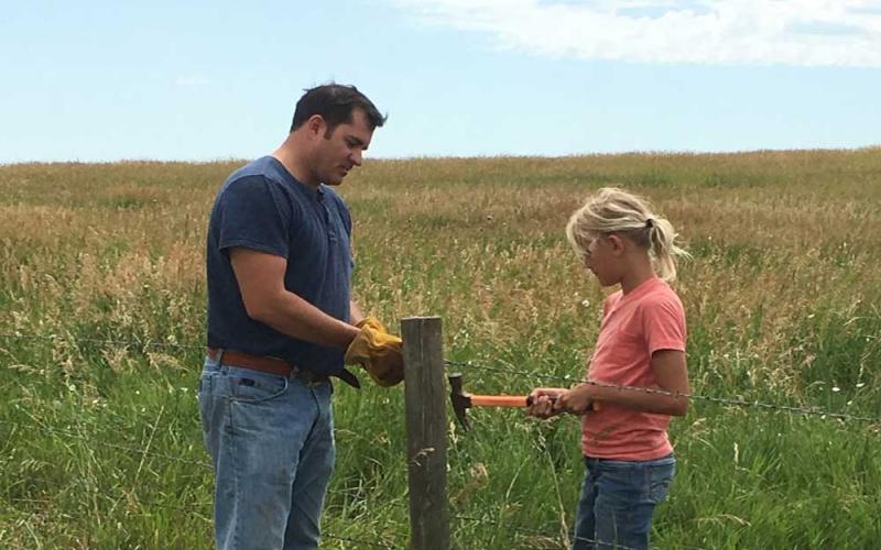 A father and daughter working on a fence along rangeland.
