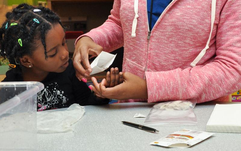 Teacher pouring a small amount of seed into a student's hand to construct a tiny greenhouse.