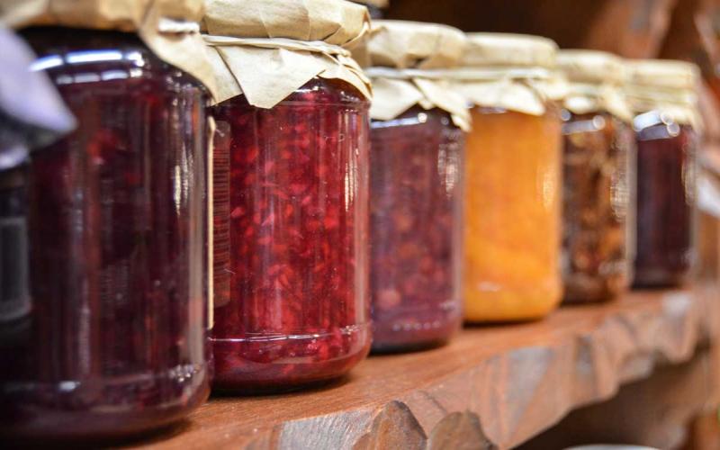 Several jars of canned jellies lined up on a pantry shelf.
