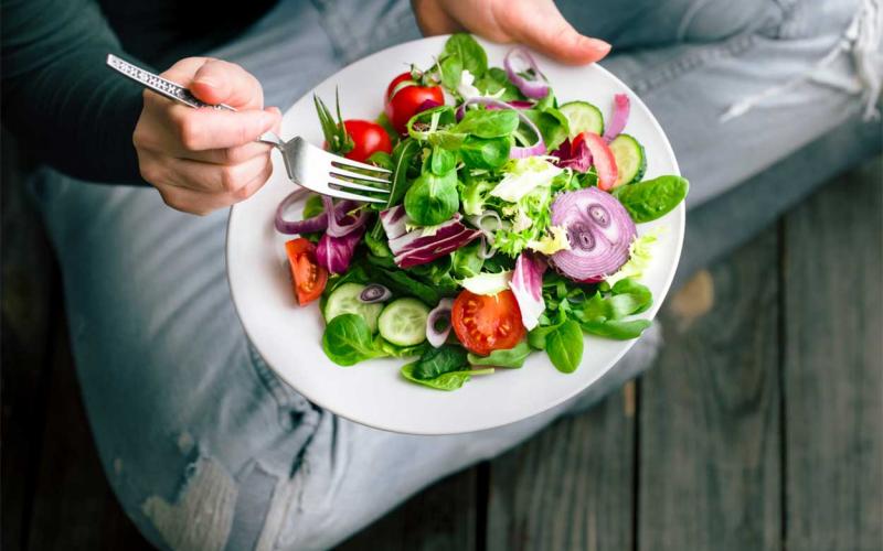 Young woman sitting with a plate of salad in her hands.