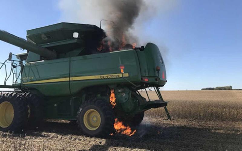 A green combine that has caught fire in the field.