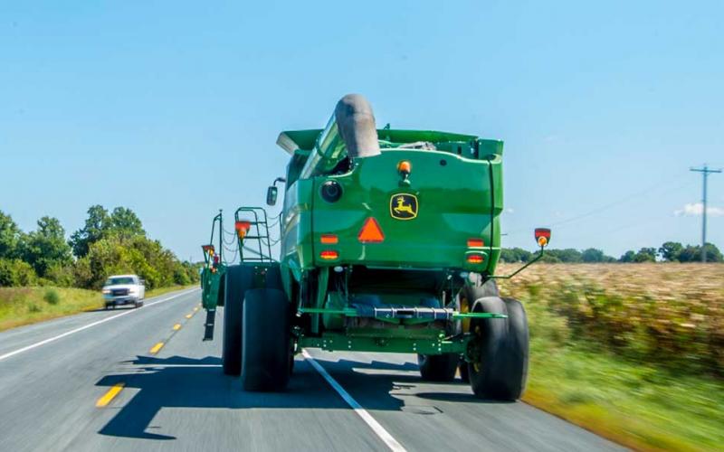 A green combine driving down a paved road.
