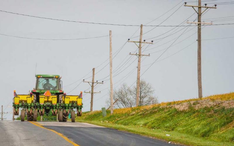 Green tractor driving down a road with low-hanging powerlines across it.