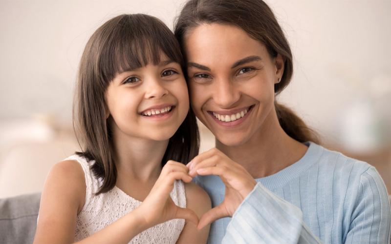 Daughter and happy mother join hands in heart shape.