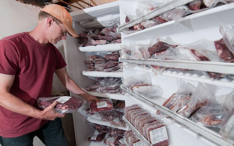 Producer inspecting an inventory of farm-raised, frozen beef in a freezer.