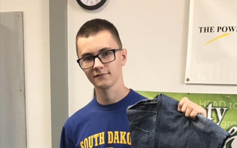 a young man standing in front of a stack of blue jeans, holding a pair of blue jeans up.
