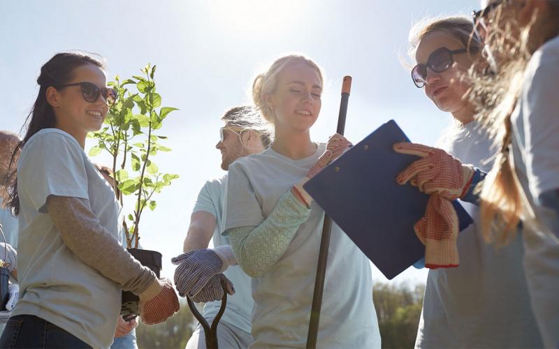 Woman with clipboard instructing a group of volunteers in a community garden.