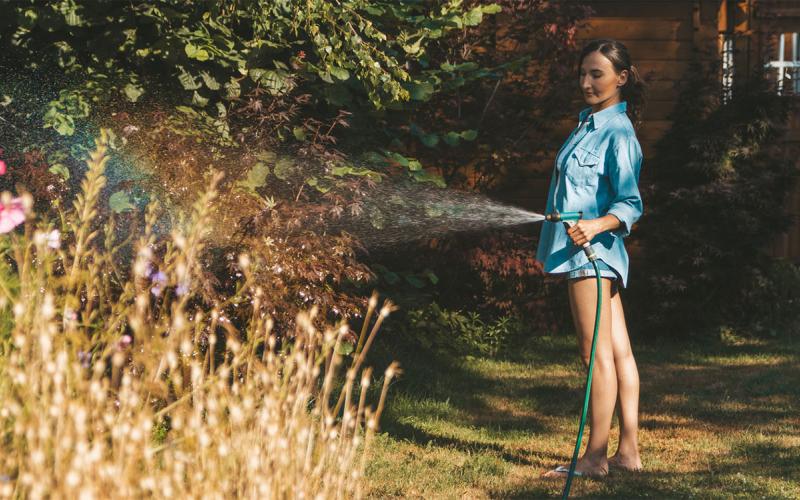 Young woman watering a drought-stressed flower garden.