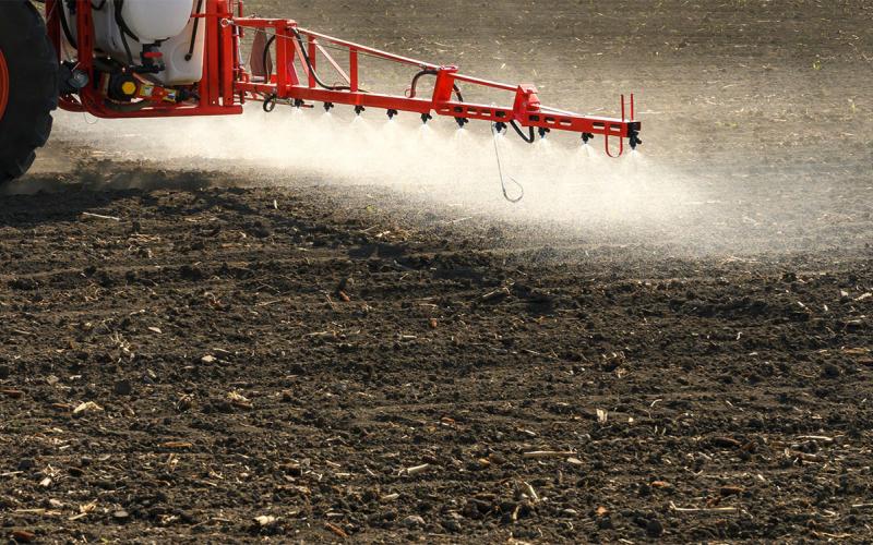 Tractor spraying pre-emergent herbicide in a bare field.