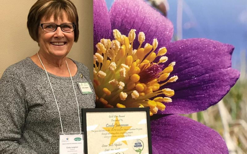 Cindy Jungman holding an award in front of an SDSU Extension Master Gardener Program banner.
