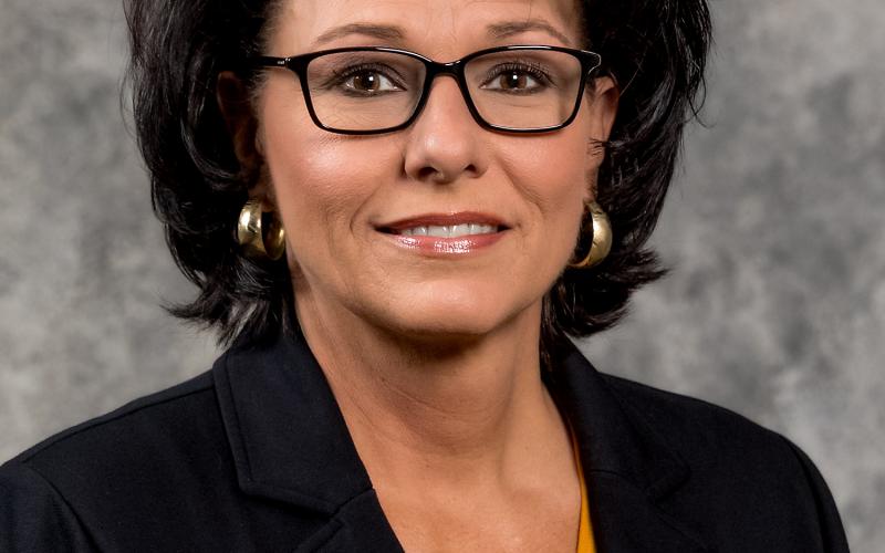 a woman with black hair wearing a black blazer and a mustard shirt