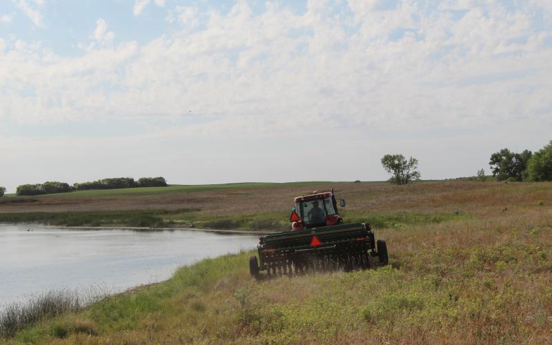 a tractor driving in a field next to a pond