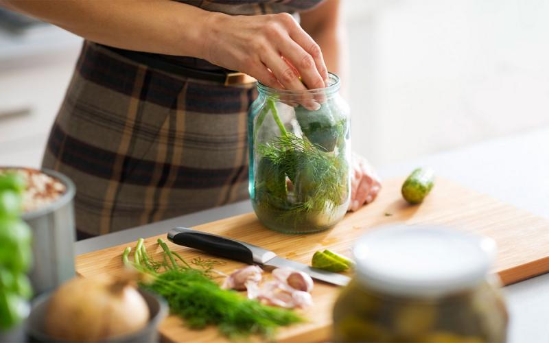 A woman preparing a jar of pickled cucumbers in a kitchen.