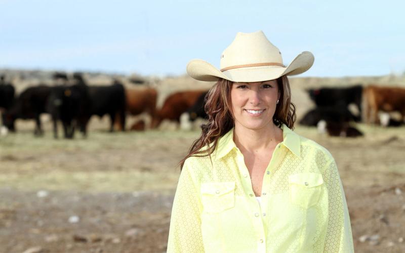 Female rancher standing in front of a cowherd.