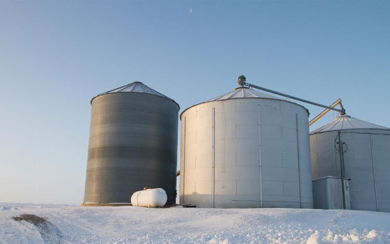 Three grain bins on the edge of a snow-covered field.