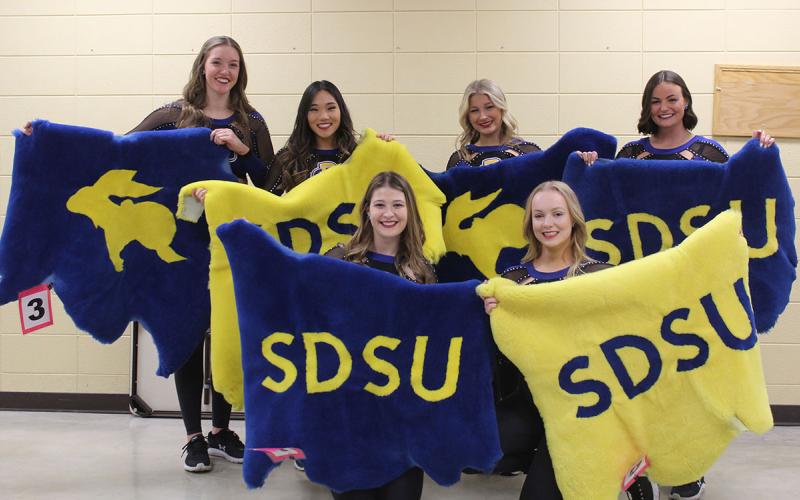 SDSU cheerleaders showcasing SDSU-themed lamb pelts for auction.