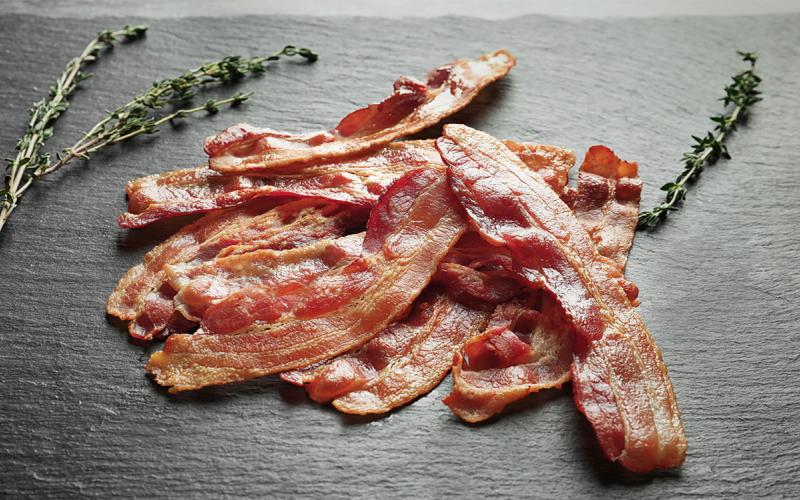 Cooked slices of bacon on a slate with fresh herbs.