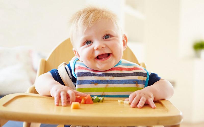 Baby seated at a highchair with a variety of soft, cut-up foods on its tray.